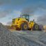 Yellow wheel loader working among large piles of crushed aggregate at a quarry and recycling site.